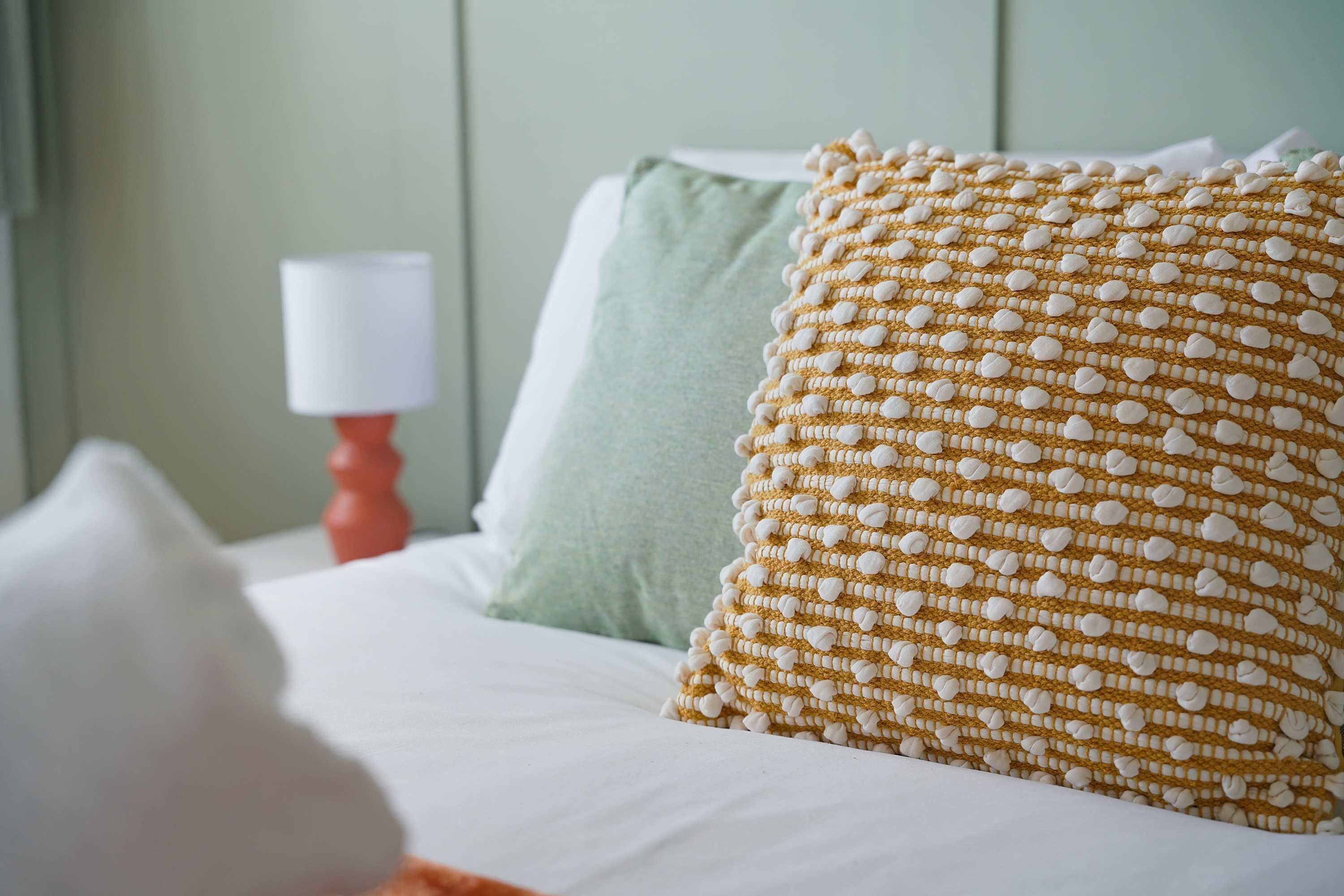 A bed with white bedding and two pillows, one with a textured pattern and the other plain.