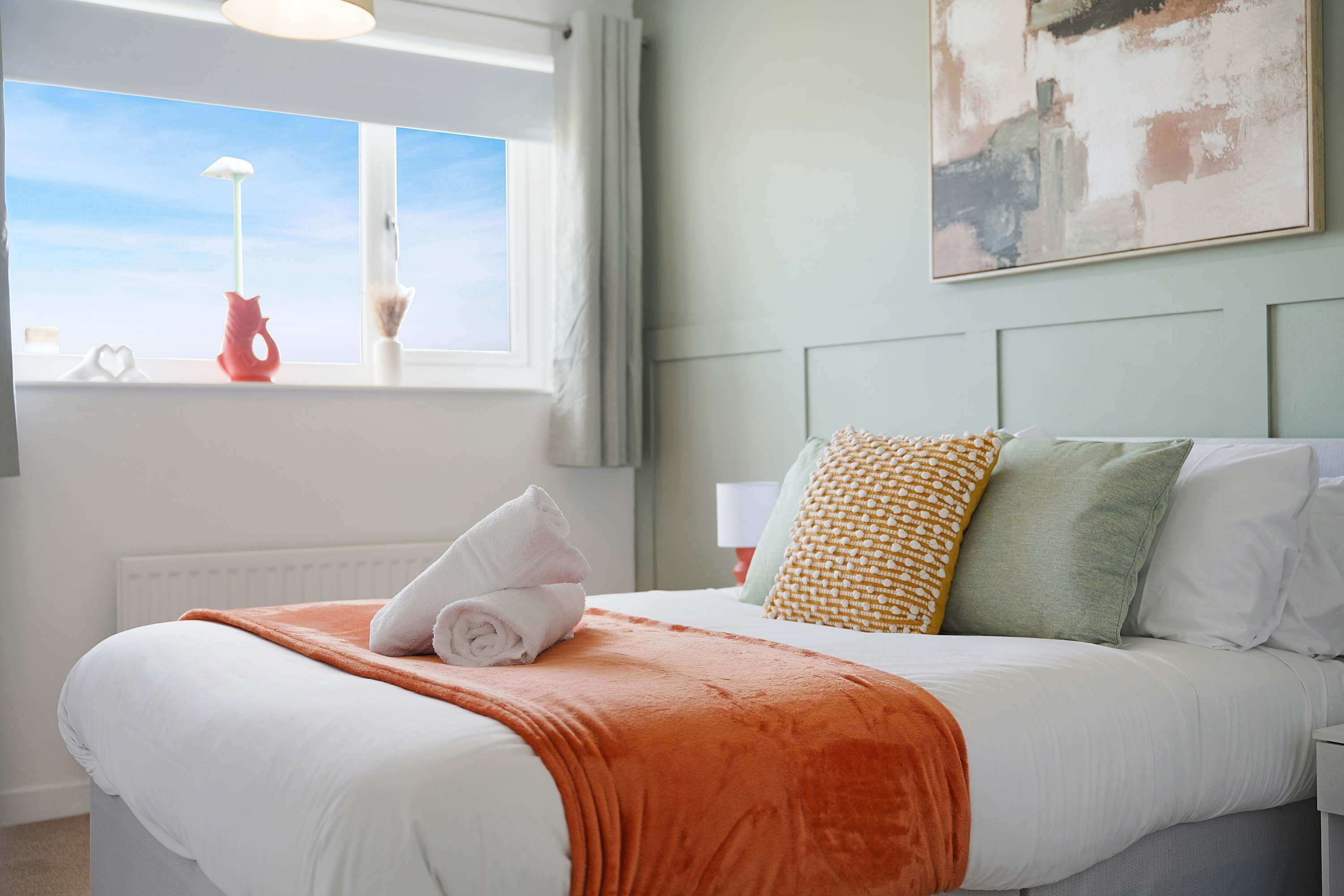 A neatly made bed with a white duvet, an orange throw blanket, and a set of pillows.