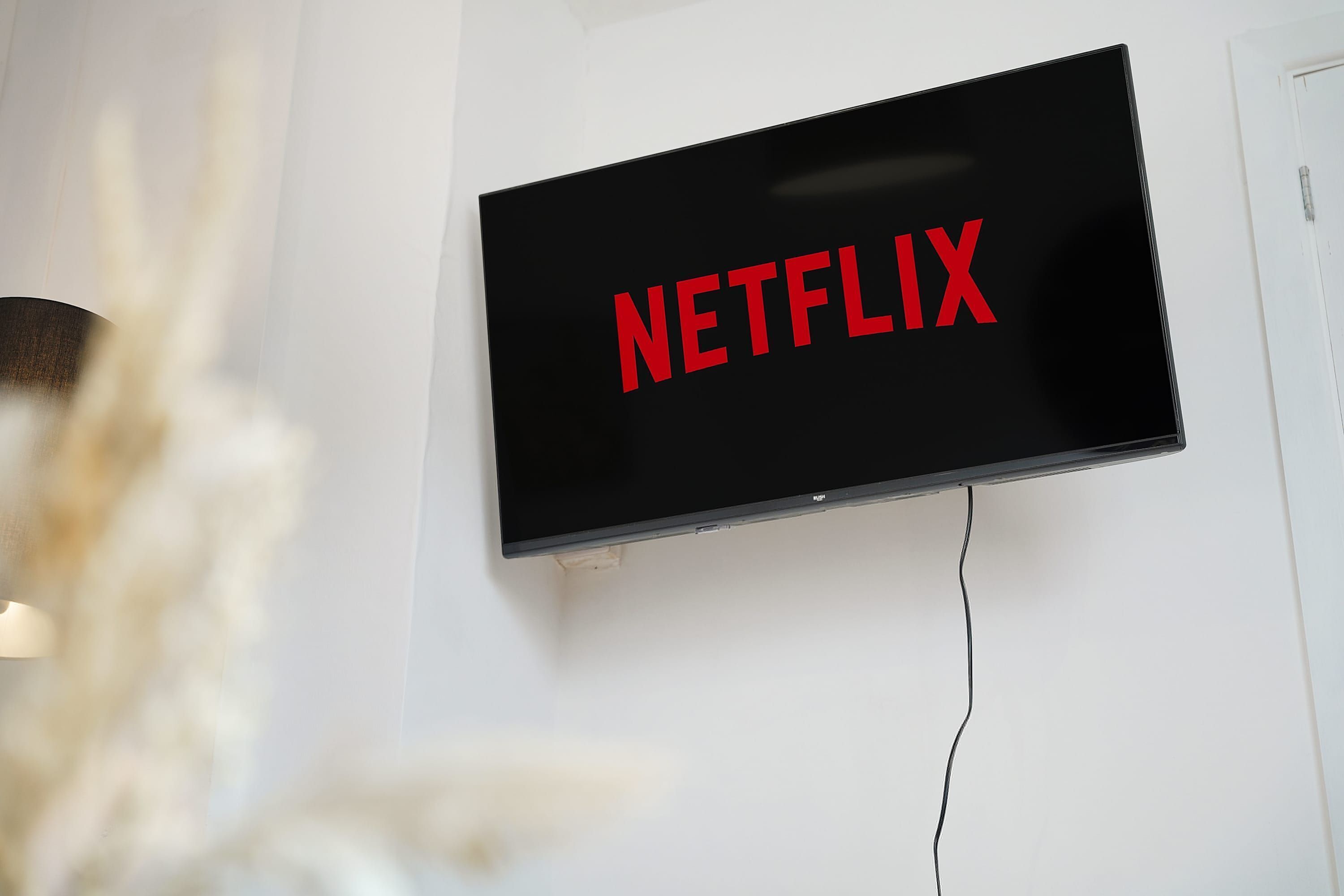 Ein Flachbildfernseher an einer weißen Wand, mit dem Schriftzug 'NETFLIX' in roter Schrift.