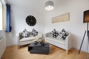 A modern living room with two sofas, a coffee table, a wall clock, and a pendant light. - Spacious 4BR Home Sleeps 8 by Stay With Us (Consett)