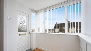A room with a white door, a window with vertical blinds, a doormat, and a view of neighboring houses. - Spacious 4BR Home Sleeps 8 by Stay With Us (Consett)