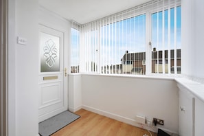 A room with a white door, a window with vertical blinds, a doormat, and a view of neighboring houses. - Spacious 4BR Home Sleeps 8 by Stay With Us (Consett)