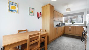 A modern kitchen with wooden cabinets, a dining table, and chairs. There are wall decorations and a window with a view. - Spacious 4BR Home Sleeps 8 by Stay With Us (Consett)