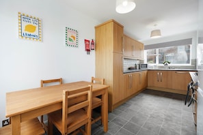 A modern kitchen with wooden cabinets, a dining table, and chairs. There are wall decorations and a window with a view. - Spacious 4BR Home Sleeps 8 by Stay With Us (Consett)