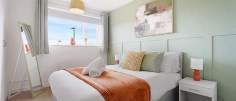 Une chambre Ă coucher avec un lit, une table de chevet, une fenĂŞtre avec des rideaux, un tableau au mur et un luminaire au plafond.