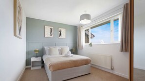 A bedroom with a bed, nightstands, a radiator, a window with curtains, and wall art. - Spacious 4BR Home Sleeps 8 by Stay With Us (Consett)
