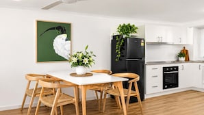 A modern kitchen with white cabinets, a black refrigerator, and a dining area with a white table and wooden chairs. - Modern Family Retreat Townsville• Walk to Mater Hospital • Parking (Pimlico)