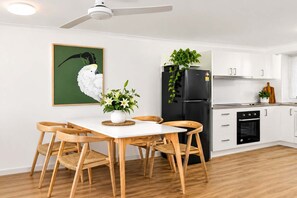 Eine moderne Küche mit weißen Schränken, einem schwarzen Kühlschrank und einem Essbereich mit weißem Tisch und Holzstühlen.