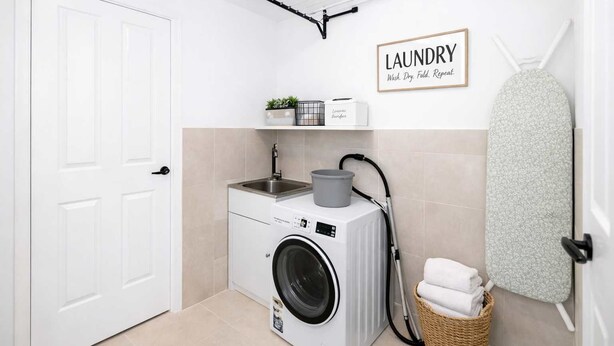 A laundry room with a washing machine, a drying rack, and a shelf with plants and a basket. - Modern Family Retreat Townsville• Walk to Mater Hospital • Parking (Pimlico)