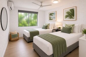 Ein Hotelzimmer mit zwei Betten, einem großen Fenster, einem Deckenventilator und einer Wandklimaanlage.