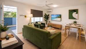 A living room with a green sofa, a dining table set for two, a ceiling fan, and a TV on the wall. - Modern Family Retreat Townsville• Walk to Mater Hospital • Parking (Pimlico)