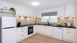 A modern kitchen with white cabinets, a black countertop, a built-in oven, and a dishwasher. - Modern Family Retreat Townsville• Walk to Mater Hospital • Parking (Pimlico)