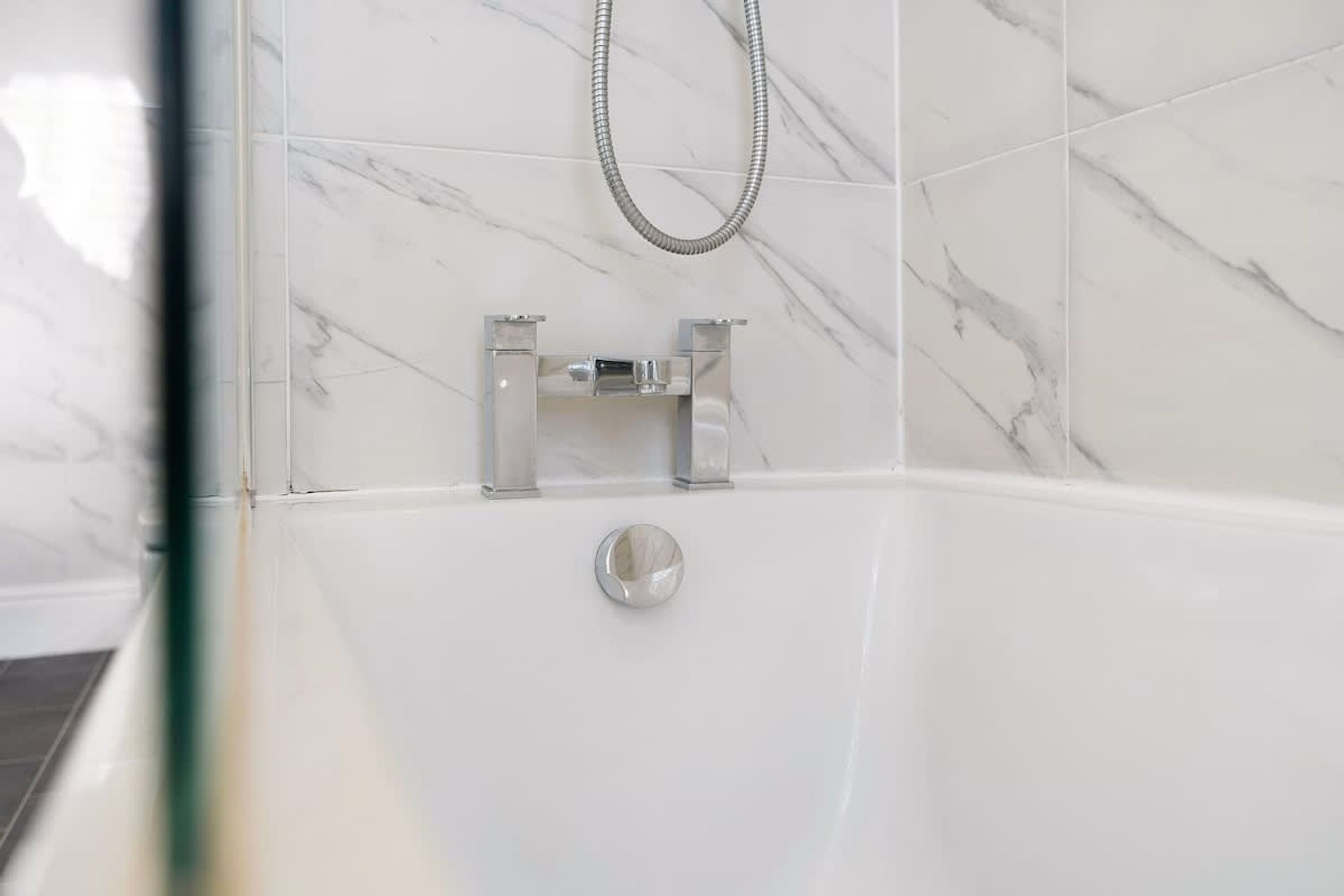 A bathroom with a white bathtub, a shower head, and a marble wall.