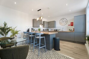 Una cocina moderna con una isla central, taburetes de bar, una mesa redonda y un reloj en la pared.