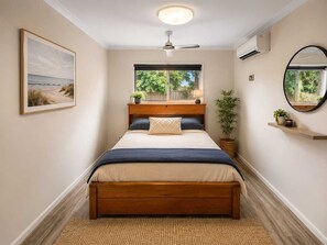 Ein Schlafzimmer mit einem Bett, einem Deckenventilator, einem Fenster, einem an der Wand befestigten Spiegel und einem gerahmten Bild.