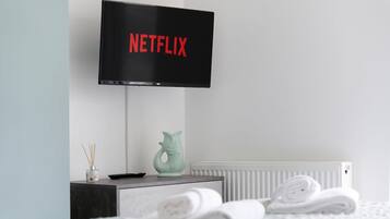 A modern room with a flat-screen TV displaying 'NETFLIX' on the screen, a small table with a decorative fish sculpture, and neatly folded towels on the floor.