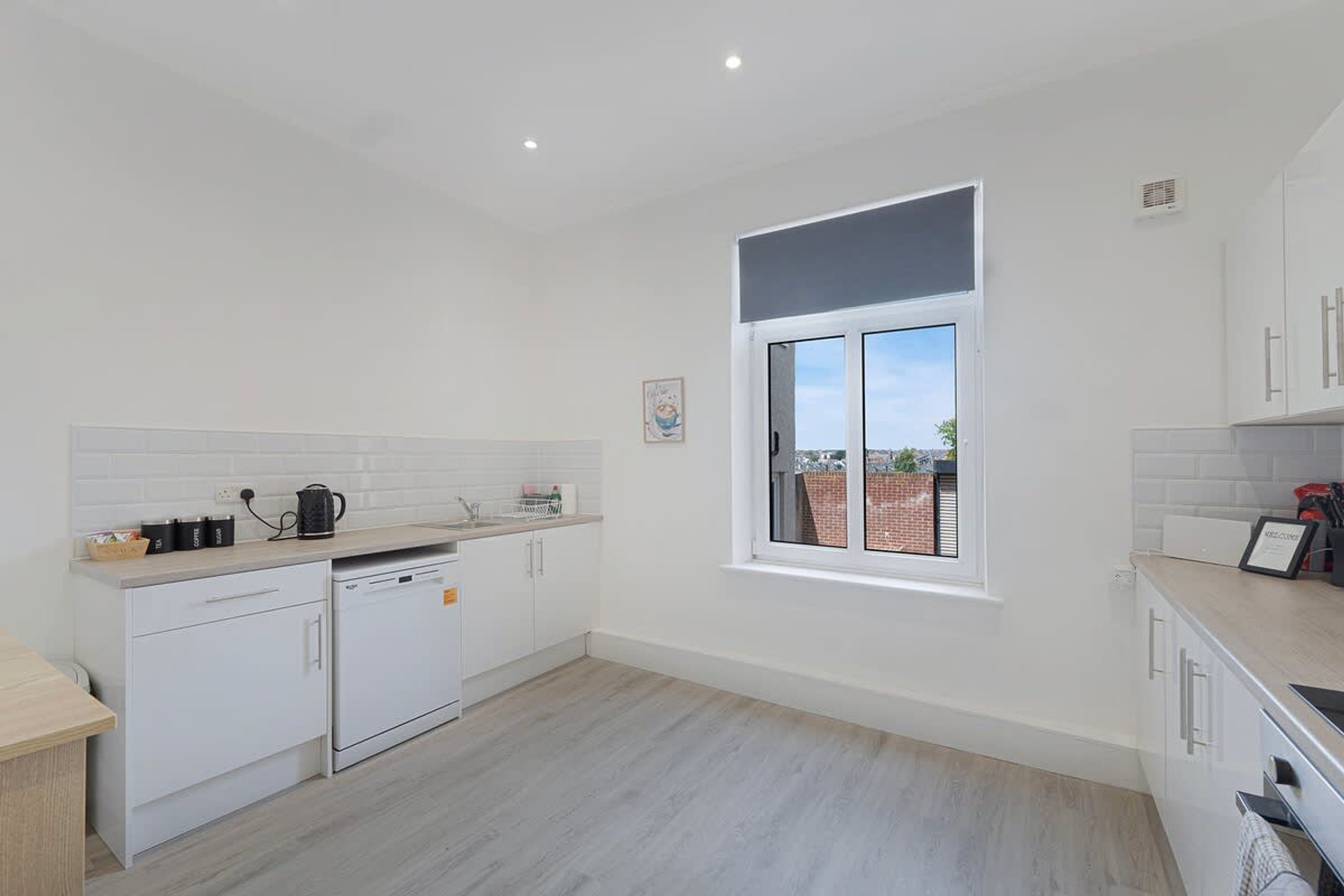 Una cocina moderna con armarios blancos, lavavajillas y ventana con vistas al exterior.