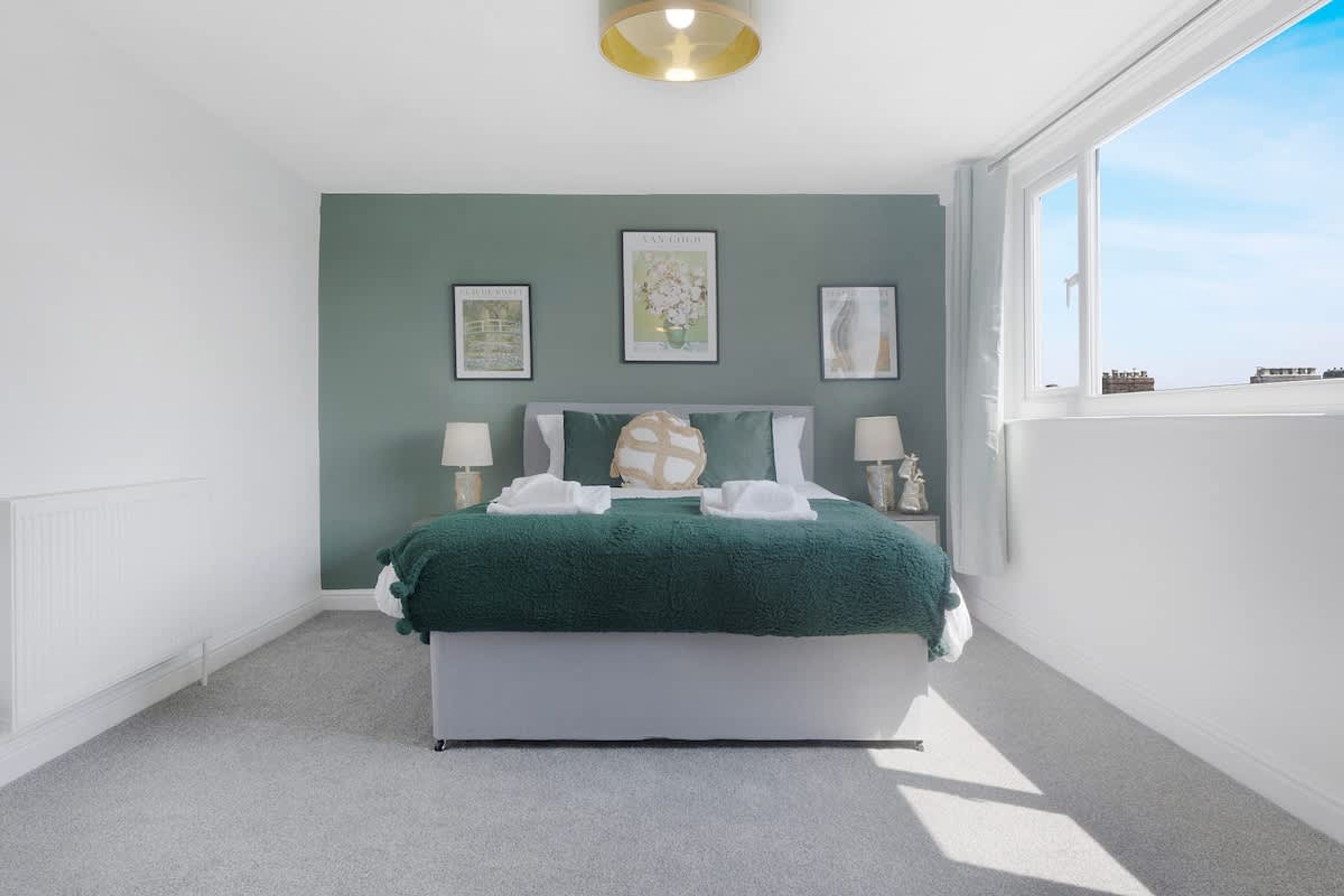 A bedroom with a bed, two bedside tables, a window, and three framed pictures on the wall.