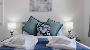 Habitación de hotel con una cama, dos almohadas, dos lámparas de noche, una decoración con forma de corazón y una toalla sobre la cama.