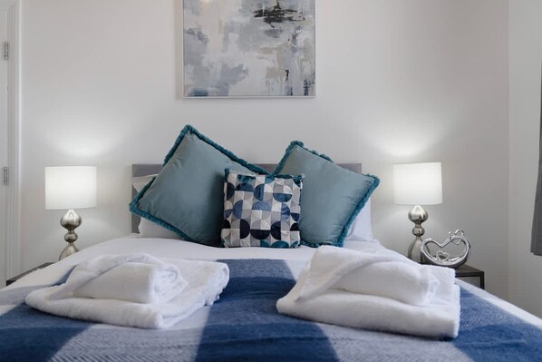 Une chambre d’hôtel avec un lit, deux oreillers, deux lampes de chevet, une décoration en forme de cœur et une serviette sur le lit.
