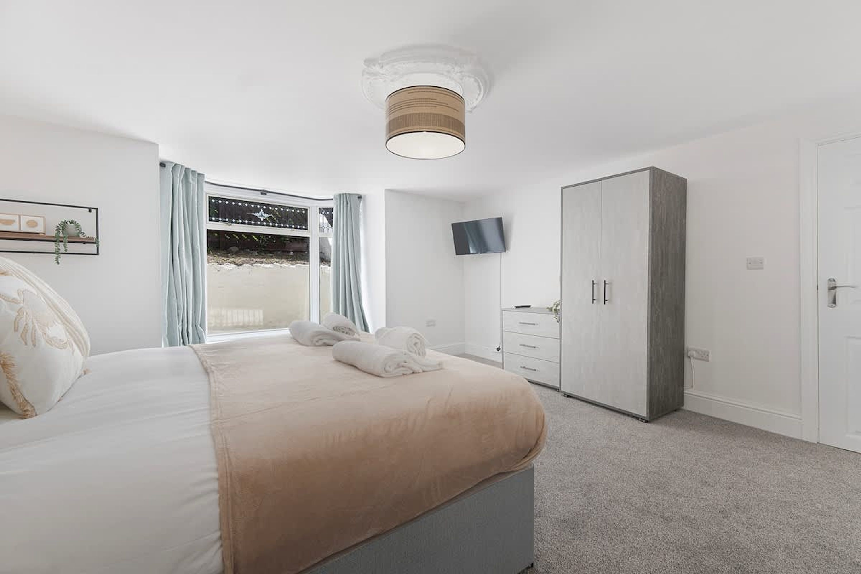 A bedroom with a bed, a wardrobe, a television, and a window with curtains.