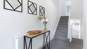 A hallway with a radiator, a wooden console table with a bowl, and three geometric wall art pieces. - Spacious 6BR Sleeps 12 With Parking (South Shields)