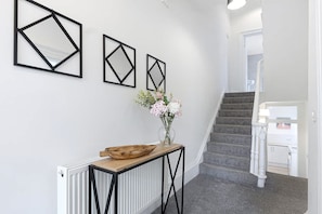 Ein Flur mit einem Heizkörper, einem Holztischchen mit einer Schale und drei geometrischen Wandbildern.