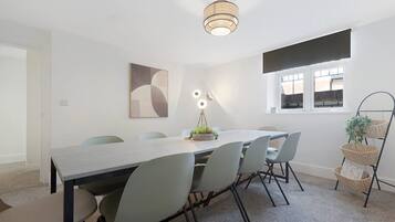 Un comedor moderno con una mesa larga, seis sillas, una lámpara colgante y un ventanal con persianas.