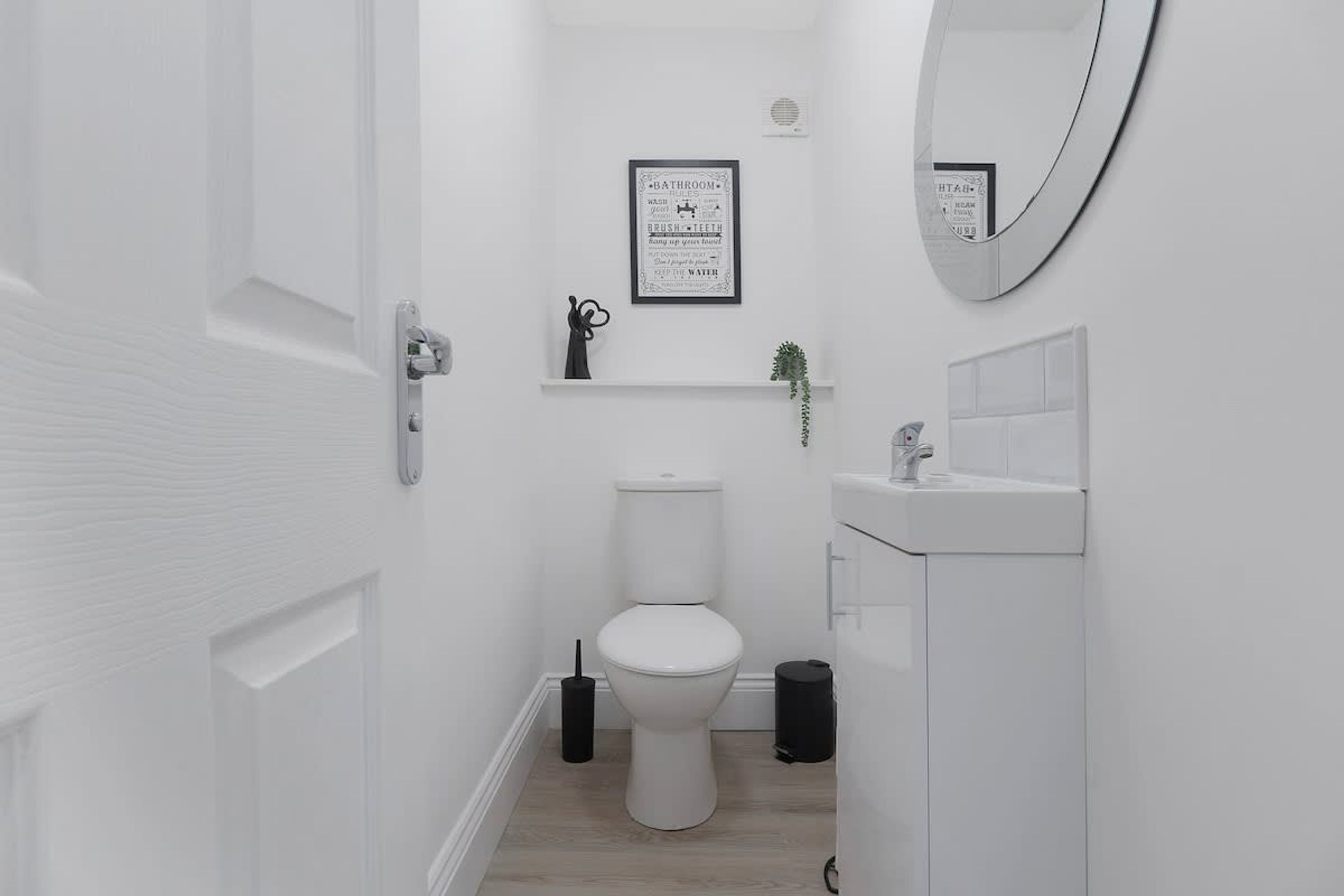 A modern bathroom with a toilet, sink, and a framed bathroom rules poster on the wall.
