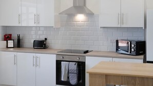 A modern kitchen with white cabinets, a stainless steel range hood, a toaster, and a microwave. - Spacious 6BR Sleeps 12 With Parking (South Shields)