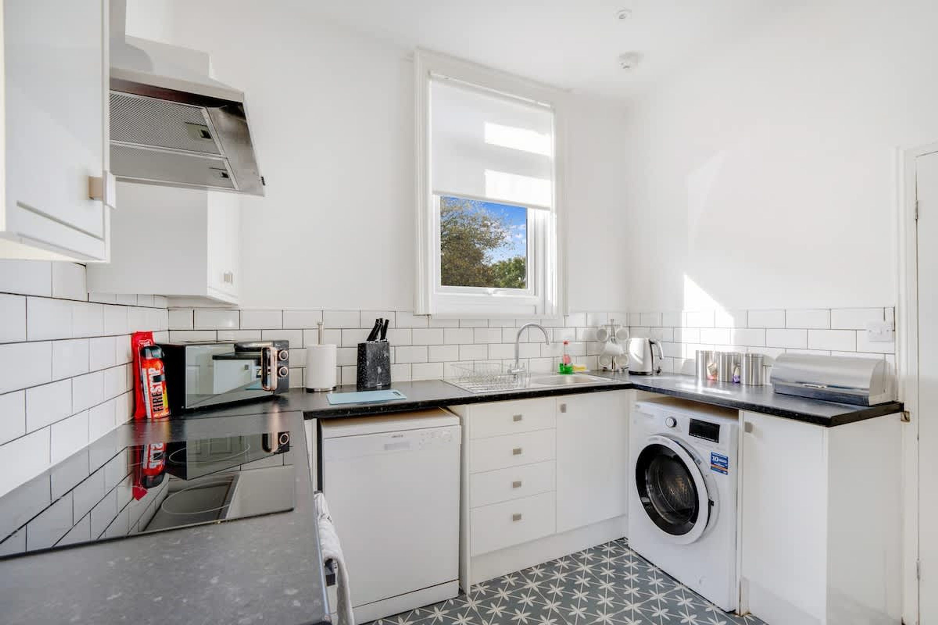 A compact kitchen with a microwave, toaster, sink, and a washing machine.