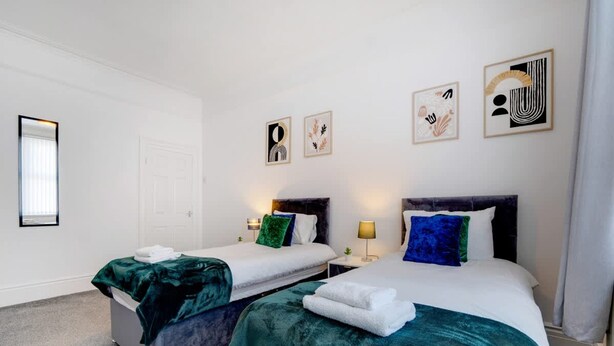Une chambre d’hôtel avec deux lits simples, une table de chevet avec une lampe et des œuvres d’art accrochées au mur.