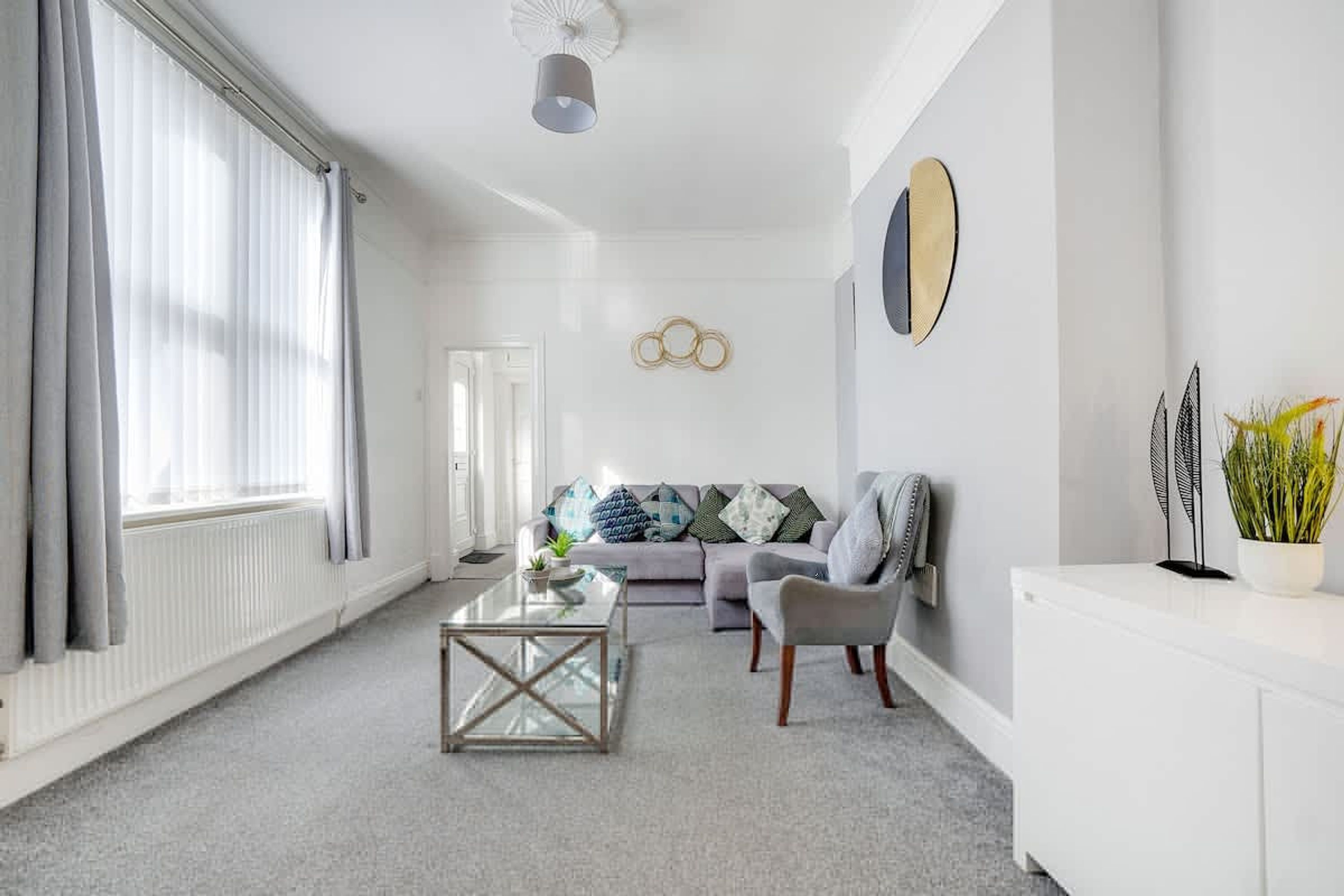 Una sala de estar moderna con una mesa de centro de vidrio, un sofá gris y un mueble blanco.