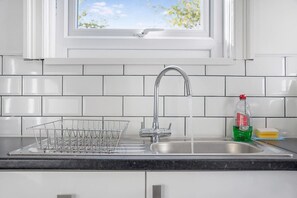 A kitchen with a stainless steel sink, a dish rack, and a window above the sink. - Family Three Bedroom Home Five Min Walk to Metro (South Shields)