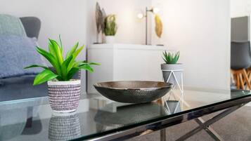 A modern living room with a glass coffee table, two potted plants, a decorative bowl, and a minimalist decor style.