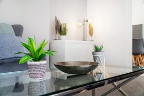 A modern living room with a glass coffee table, two potted plants, a decorative bowl, and a minimalist decor style. - Family Three Bedroom Home Five Min Walk to Metro (South Shields)