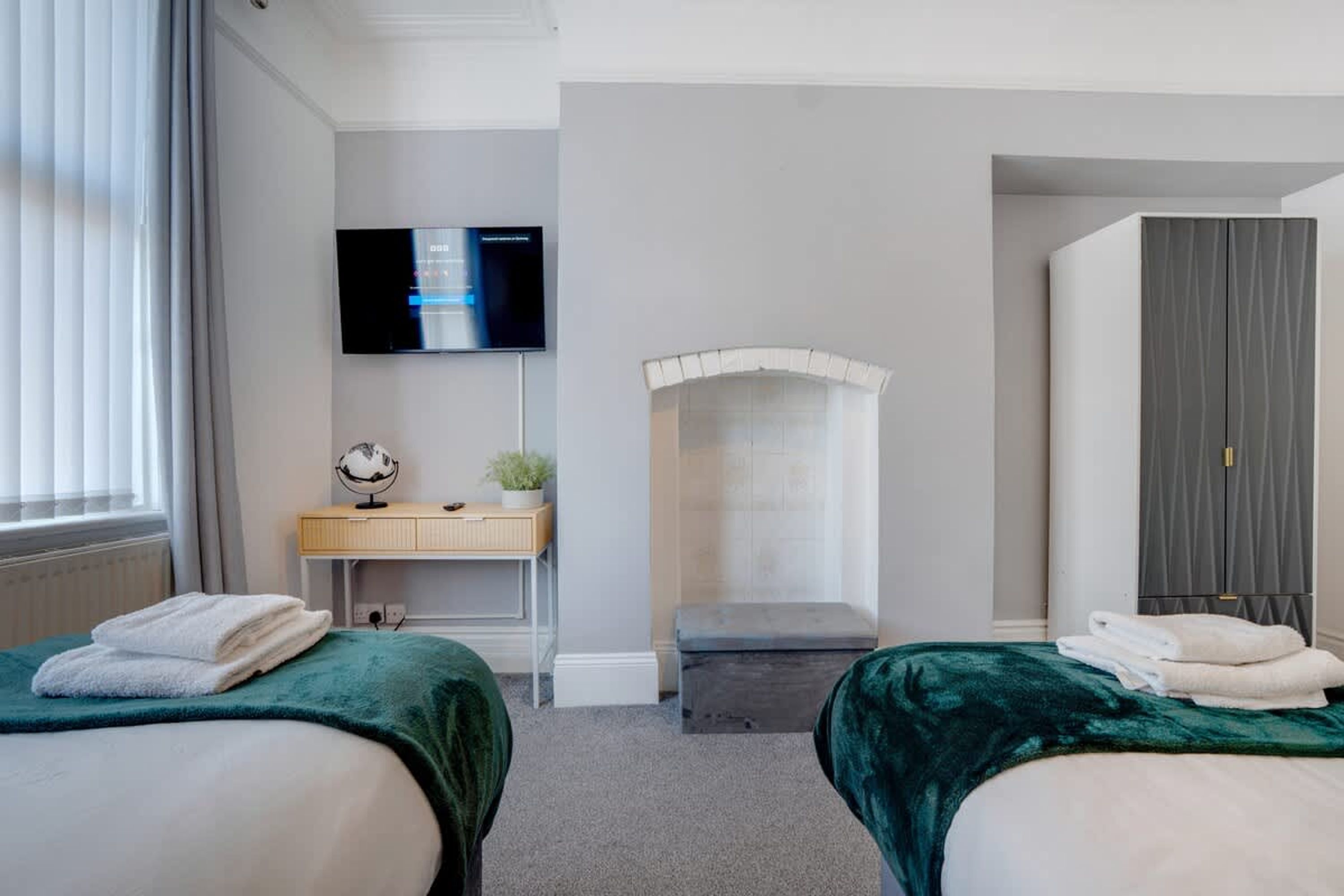Et hotelværelse med to senge, et skrivebord, et fjernsyn og en garderobe.