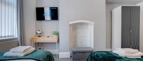 Quarto de hotel com duas camas, uma escrivaninha, televisão e guarda-roupa.