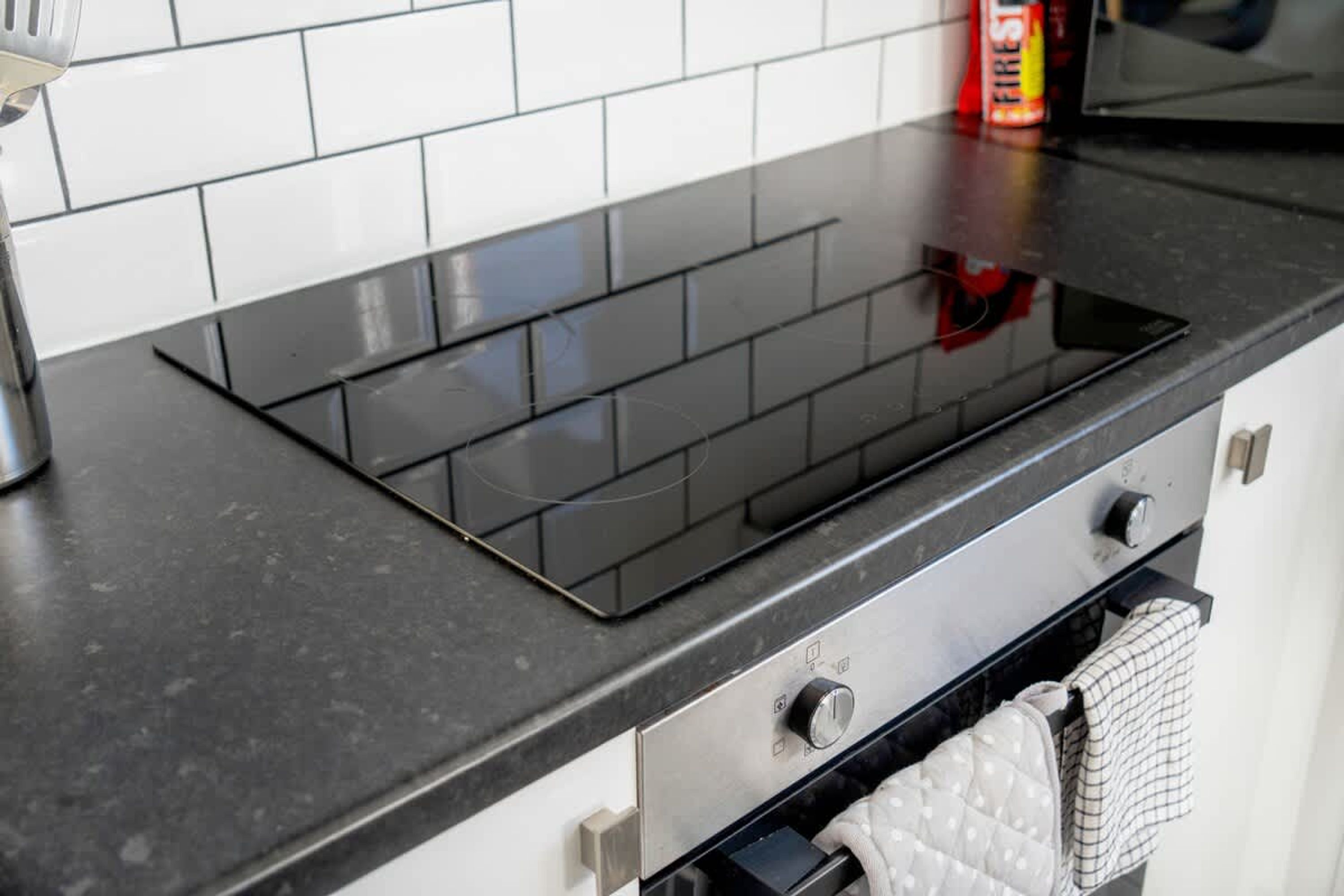 Una cocina con una placa de inducción negra, un horno de acero inoxidable y un salpicadero de azulejos blancos.