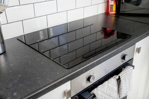 Een keuken met een zwart inductiekookveld, een roestvrijstalen oven en een witte betegelde spatwand.