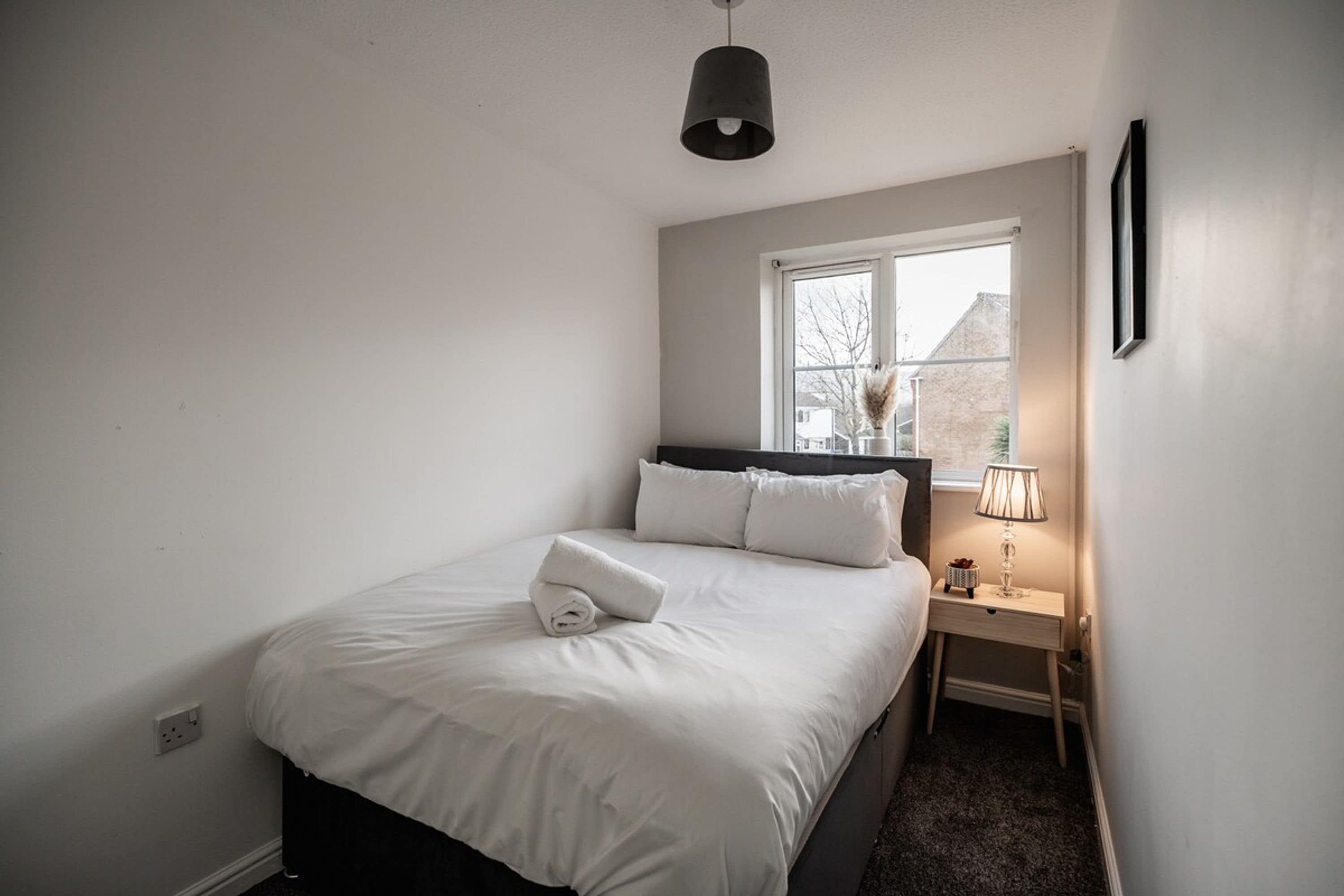 A bedroom with a bed, a window, a nightstand, and a lamp.