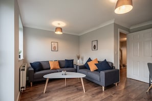 Ein modernes Wohnzimmer mit einem grauen Ecksofa, einem runden Couchtisch und zwei Pendelleuchten.