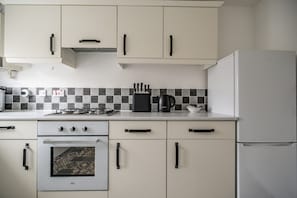 Eine Küche mit weißen Schränken, einem Gasherd, einem Wasserkocher und einem Kühlschrank.