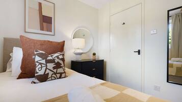 A hotel room with a bed, a bedside table with a lamp, a mirror, and a door.