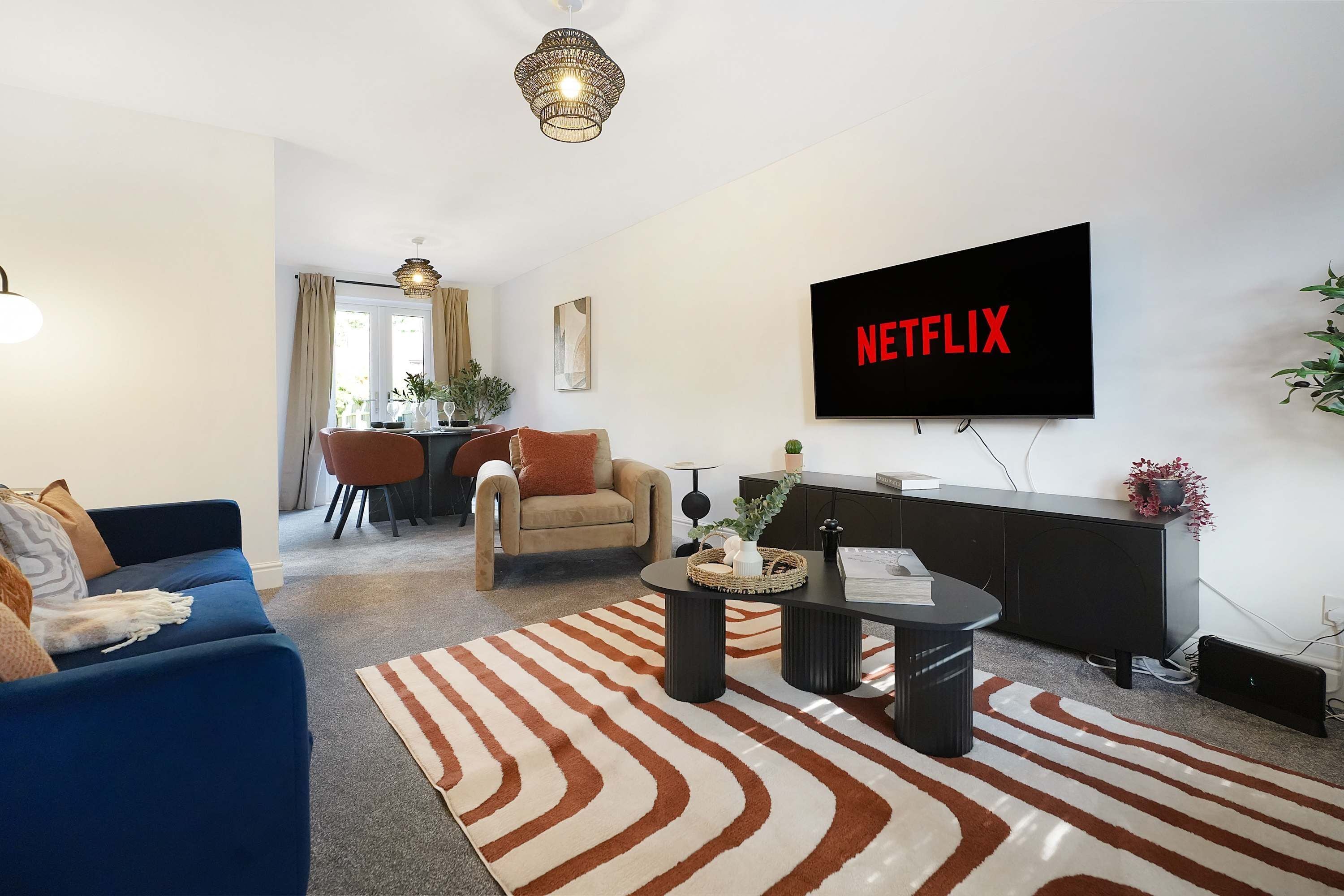 Una sala de estar moderna con un sofá, una mesa de centro, un televisor montado en la pared y un comedor al fondo.