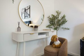 A white console desk with a round mirror, a small plant, and a teddy bear on a brown chair. - Modern 3BR Brompton Court Wi-fi By Stay With Us (Richmond)