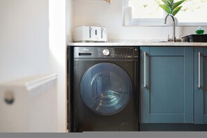 A compact washer and dryer unit with a control panel, situated in a kitchen with teal cabinetry and a window above the sink. - Modern 3BR Brompton Court Wi-fi By Stay With Us (Richmond)