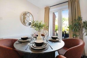 A dining area with a round table set for four, a mirror on the wall, and a view of the outdoors through a glass door. - Modern 3BR Brompton Court Wi-fi By Stay With Us (Richmond)