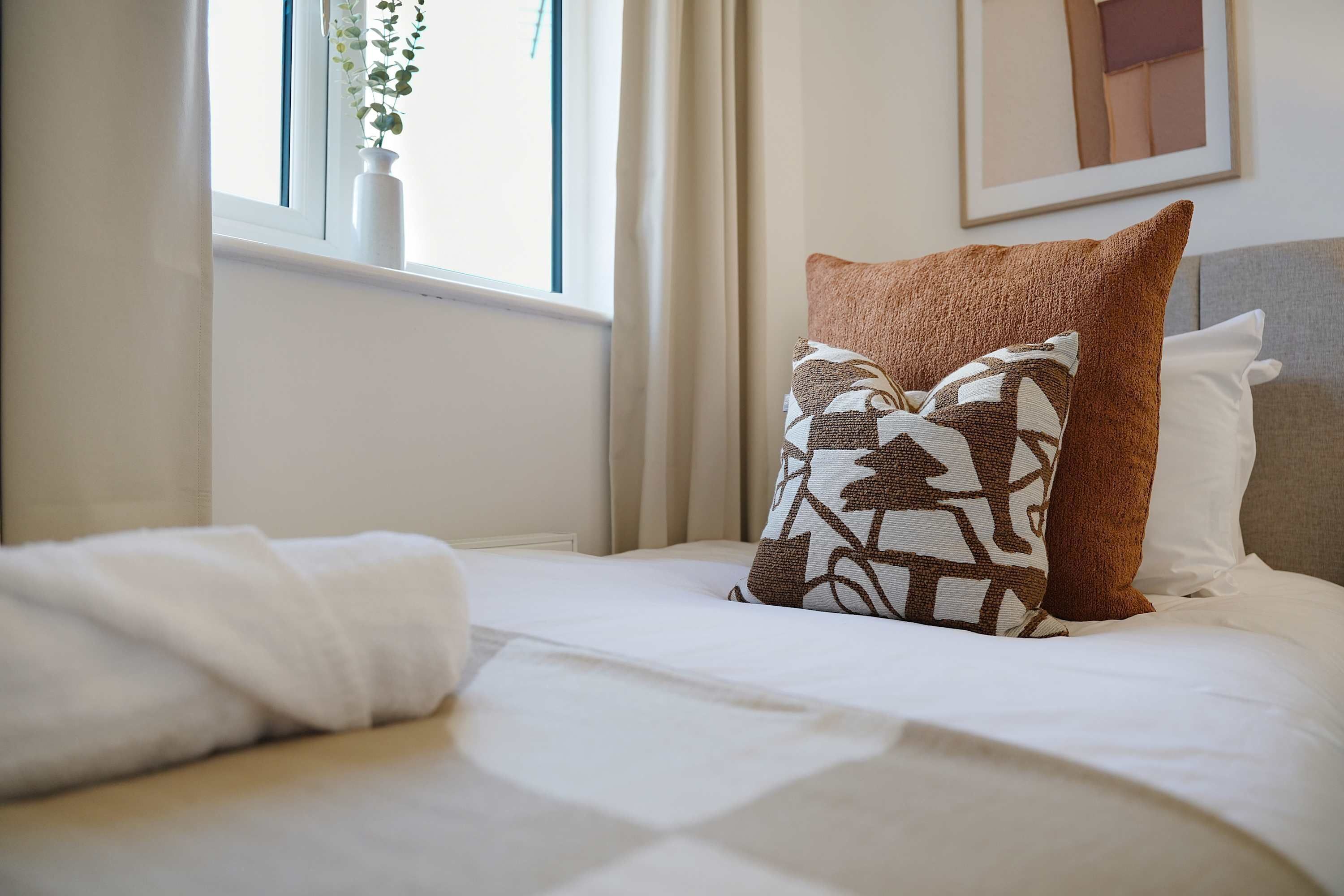 A neatly made bed with white linens, a patterned pillow, and a plain pillow.