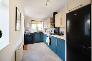 Una cocina moderna con un refrigerador negro, armarios azules, una ventana con una planta y un radiador blanco.